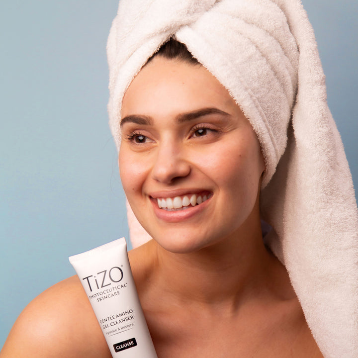 woman wearing a towel wrapped around head, holding TiZO Gentle Amino Gel Cleanser tube.