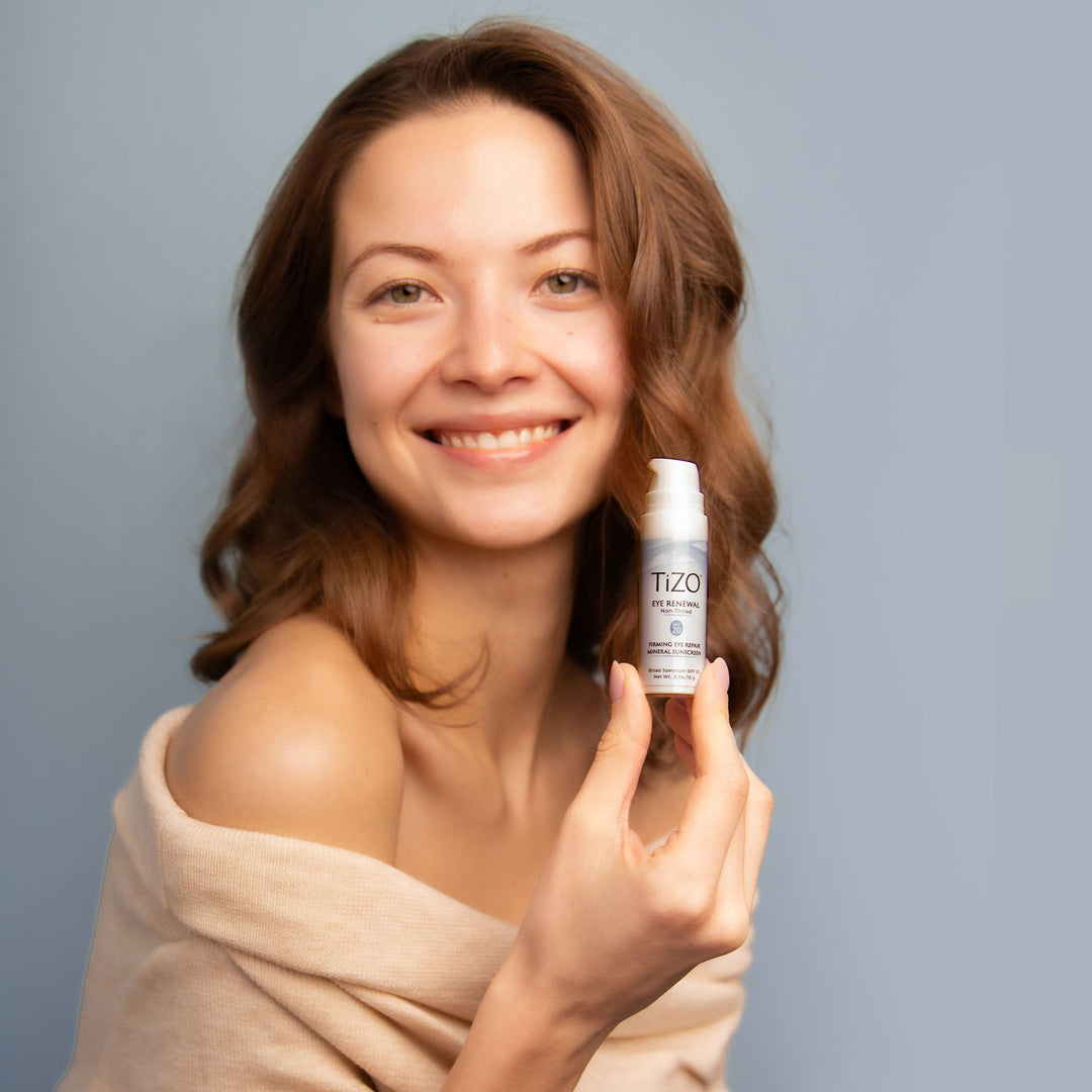 woman holding TiZO Eye Renewal Non-Tinted open cap bottle.